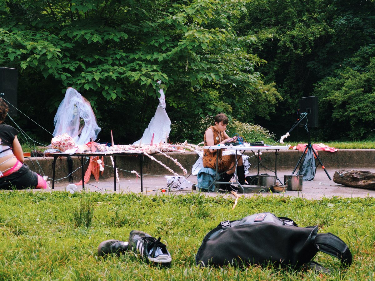 a person sitting at a table outdoors in a park performing music with electronic instruments