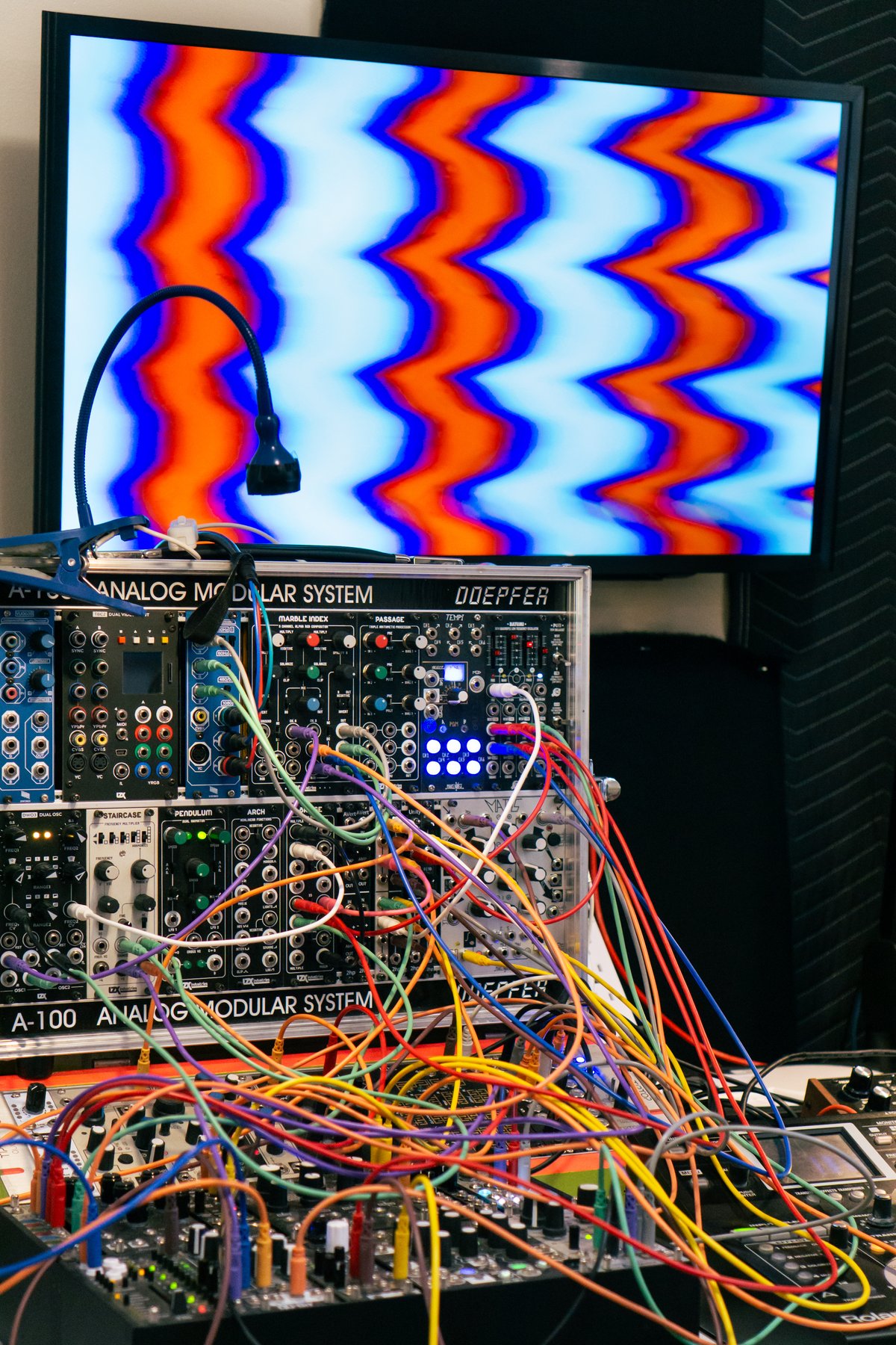 modular synth with a tv above it showing wavy blue and red lines