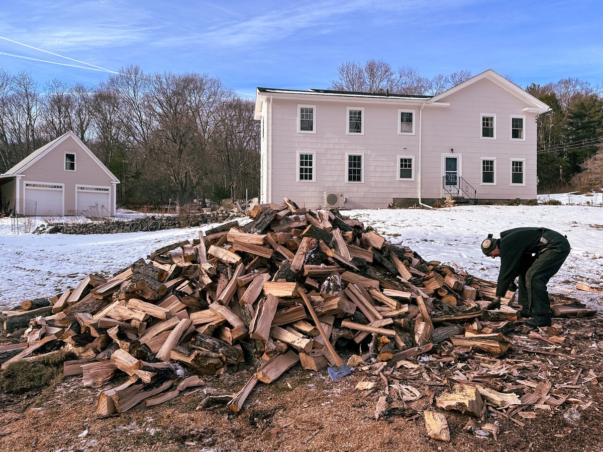 a large pile of split logs in front of a white house