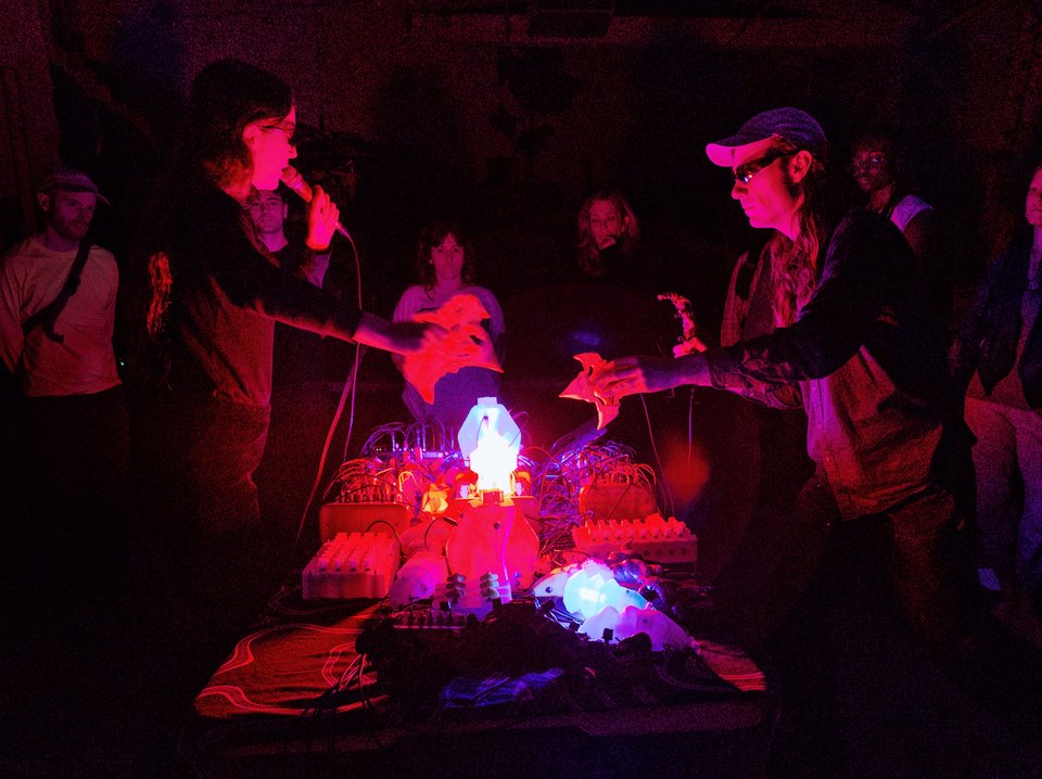 two people performing at a table covered with glowing electronic objects