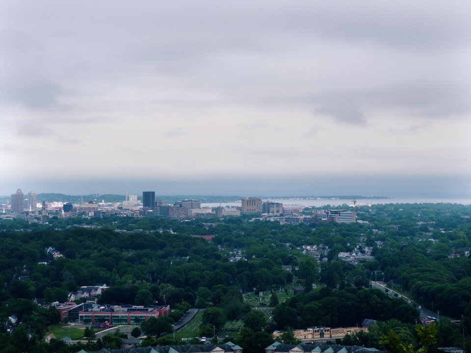 a view of new haven from a high cliff. lots of trees, a few taller buildings in the distance, then a body of water. the weather is cloudy
