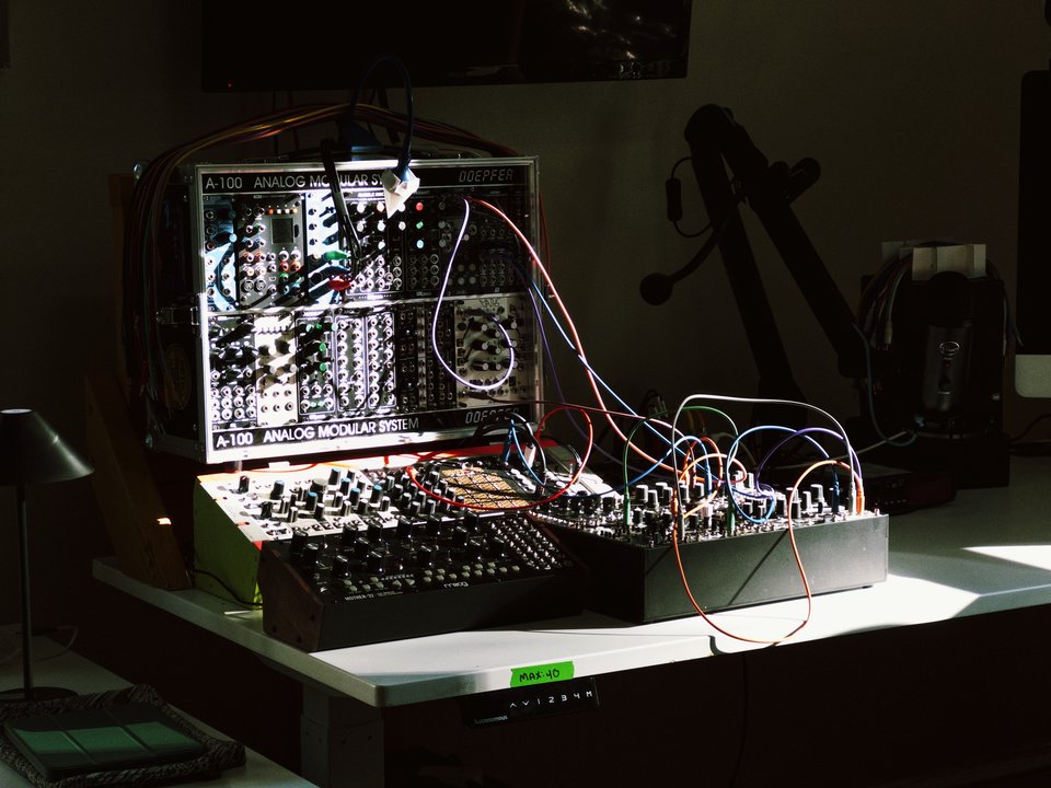 a pile of modular synths with a ray of sunlight falling on it, creating highly contrasted shadows of knobs and wires