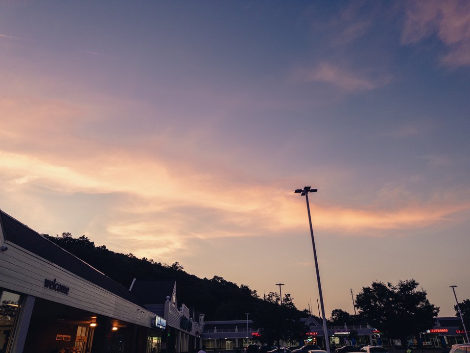 a nice skyscape of pink and purple clouds over an ugly landscape of shops and cars