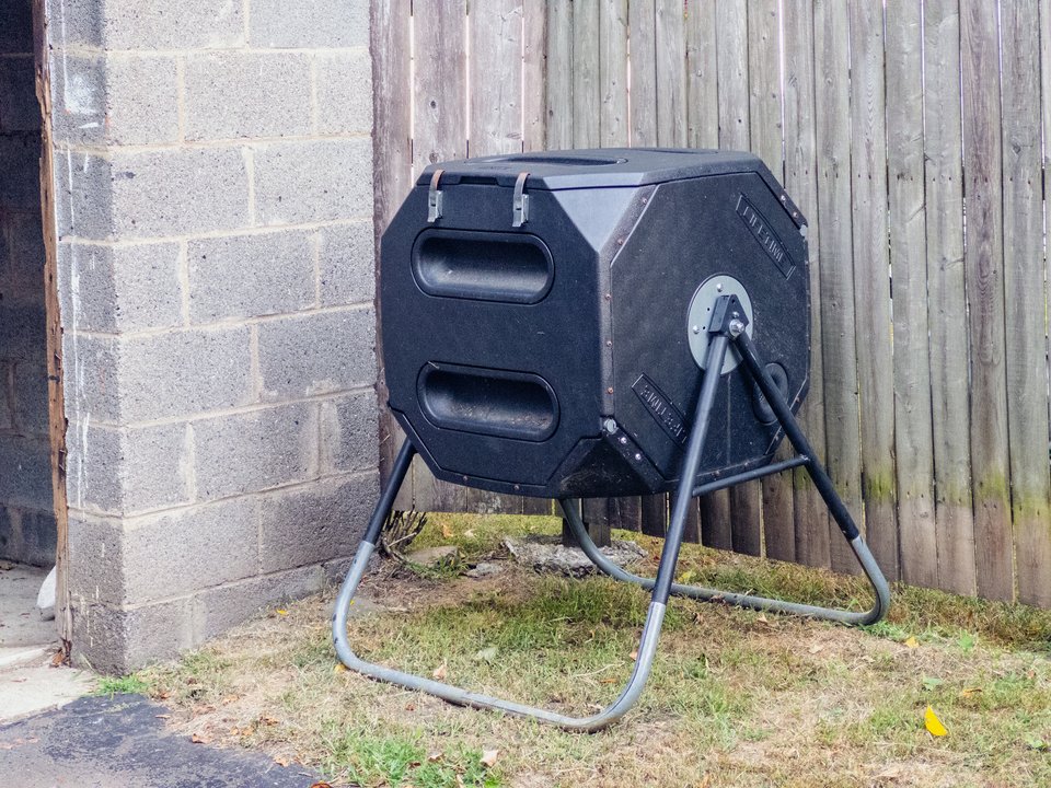a black plastic compost spinner device in a yard next to a fence and cinder block wall