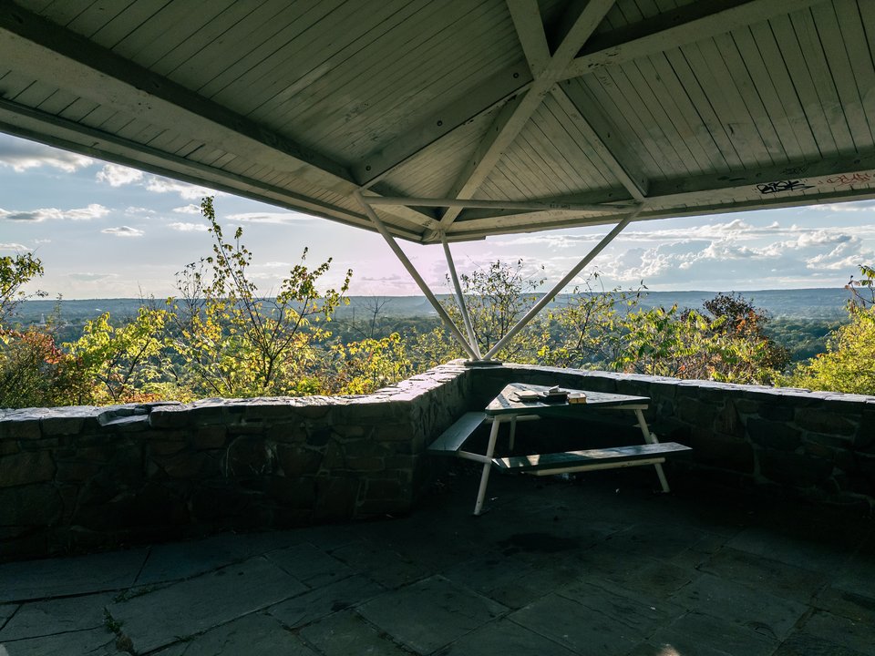 view off the edge of an overlook through a pavilion with a stone floor and wooden roof