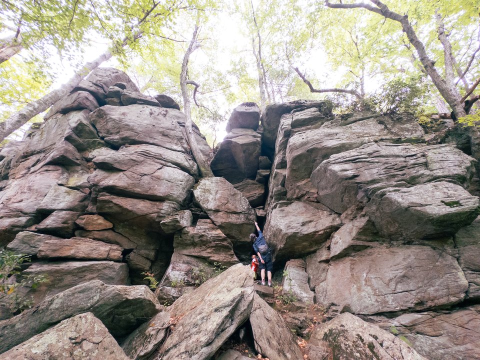 two people standing at the base of a huge stack of boulders, and looking very small in comparison