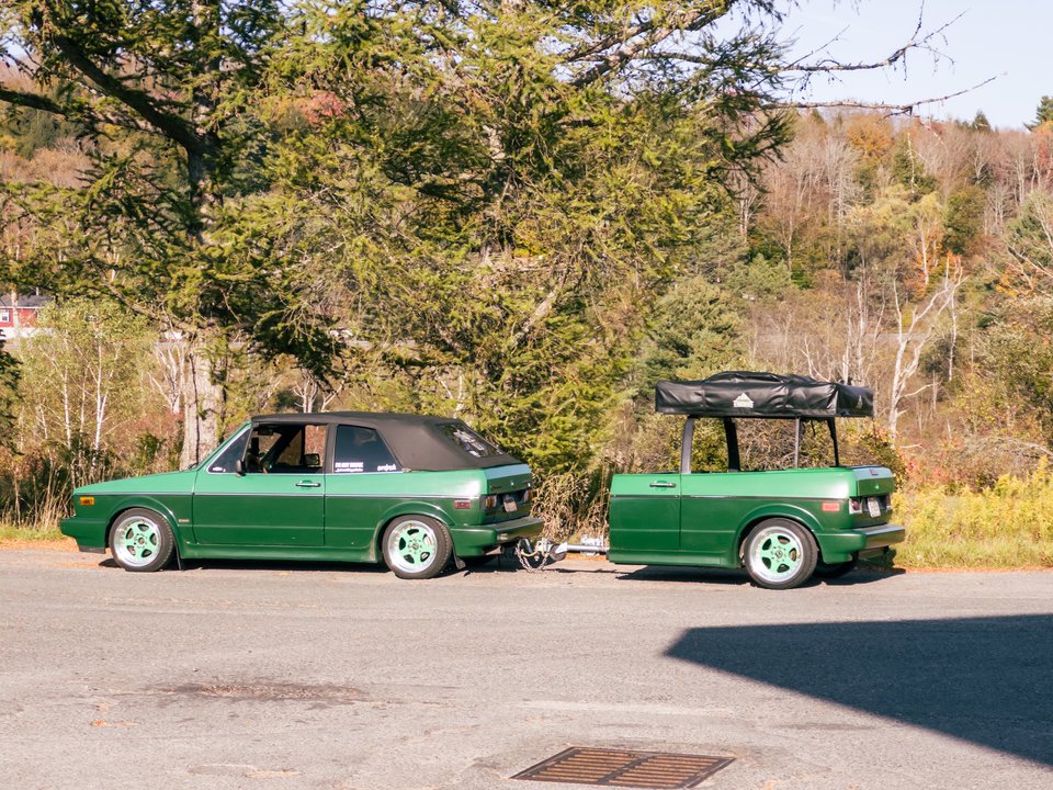 a small green convertible car pulling a trailer made from the same model of car with the front cut off
