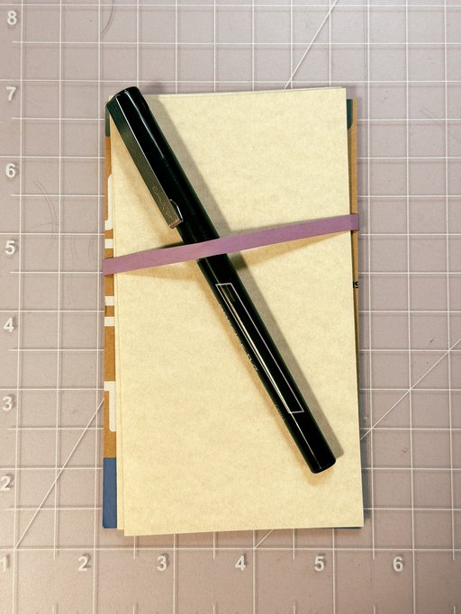 some leaves of paper secured to a pen with a rubber band
